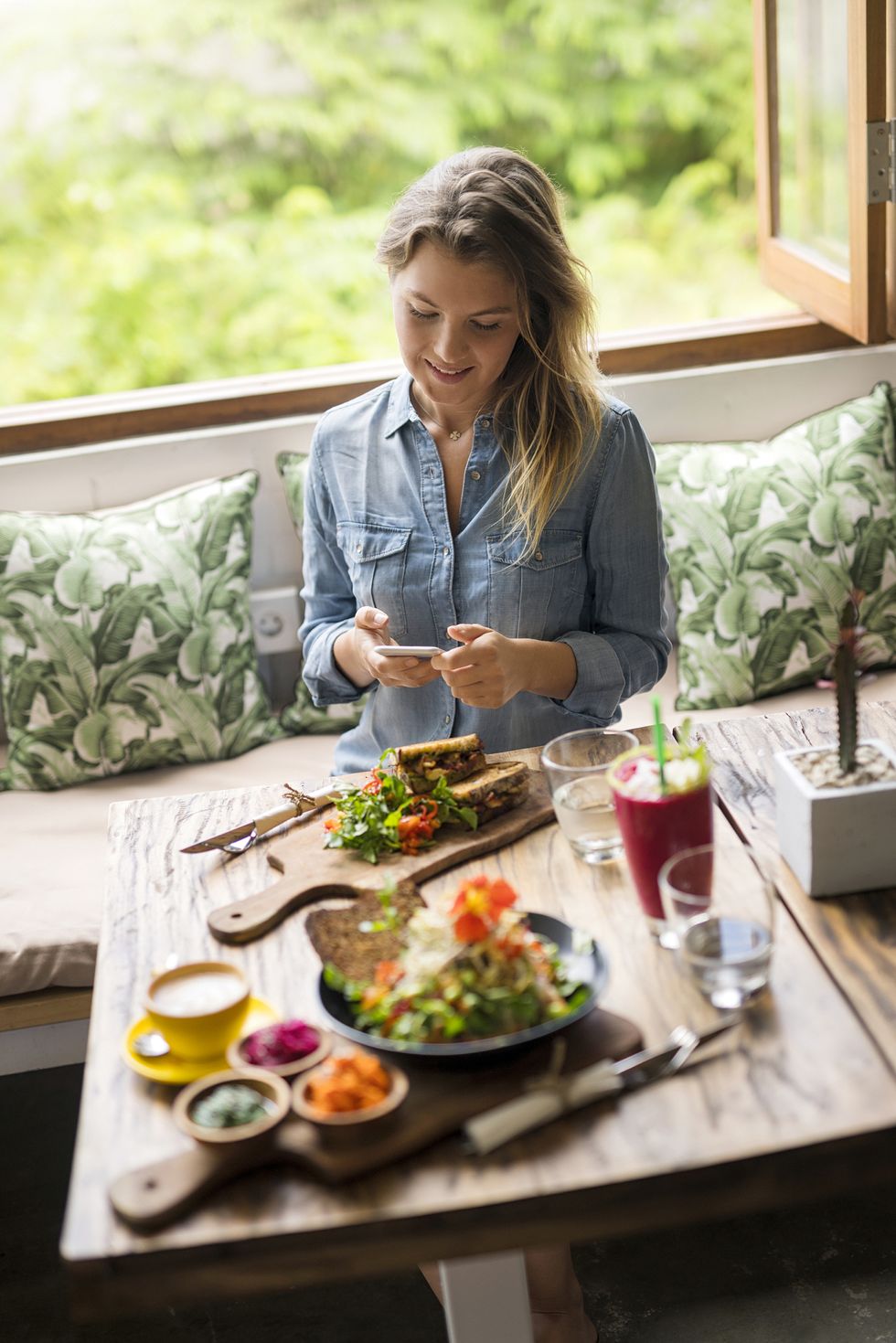 woman taking a picture of food with smartphone in cozy cafe in front of window