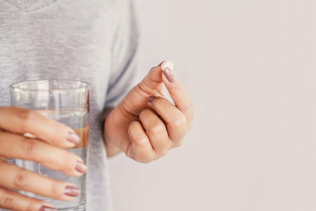 woman holding a glass of water and white pill