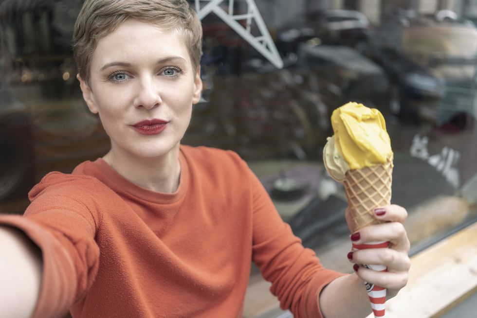woman taking selfie with ice cream in front of shop