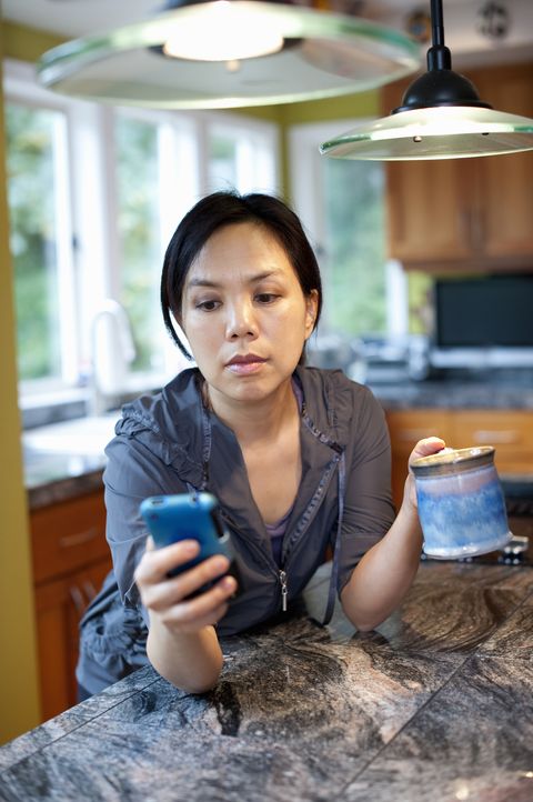 Woman checking cellphone in kitchen with coffee