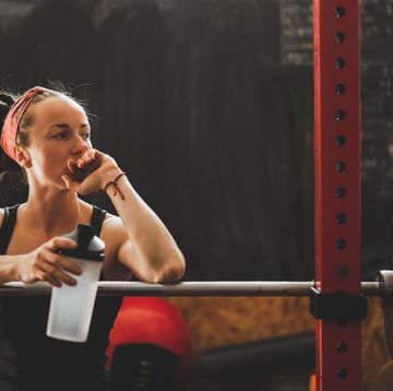 woman tired after weightlifting workout and holding reusable bottle with drinking water
