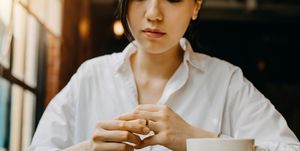 Woman touching the wedding ring on her finger nervously while having coffee and waiting in cafe