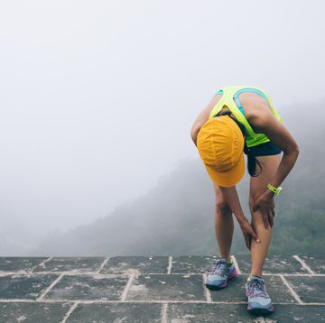 woman trail runner hold her sports injured legs at the top of mountain