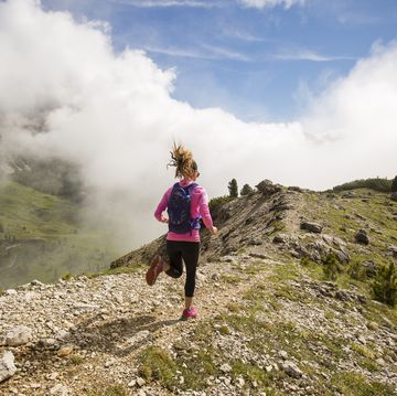 a woman trail running a path leading towards the mountains