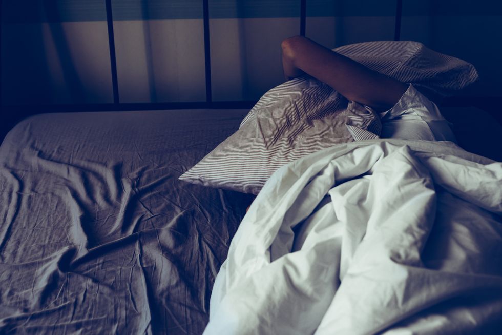 a woman trying to sleep more, having trouble sleeping due to noise, covering her ears with pillow 