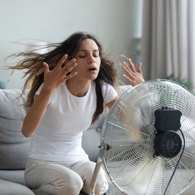 woman turned on fan waving her hands to cool herself