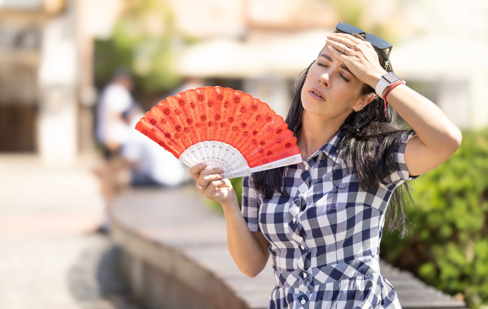 woman uses hand fan to cool down when summer heat wave hits the city