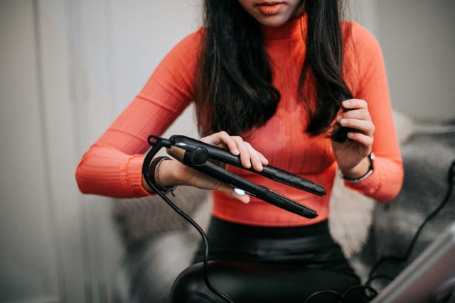 woman using hair straightener at home