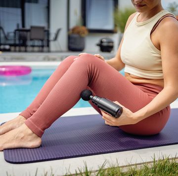 woman using massage gun after exercise by poolside in summer setting