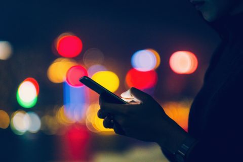 woman using mobile phone against illuminated city lights at night
