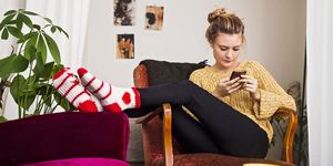Woman using phone while resting on chair at home