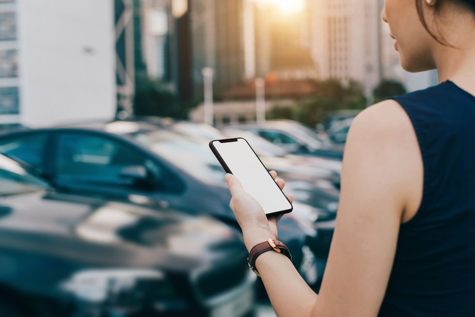 Woman using smartphone while walking to her car in outdoor car park in city