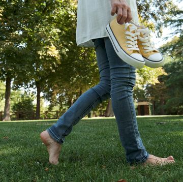 woman walking barefoot on grass, holding her sneakers lower section