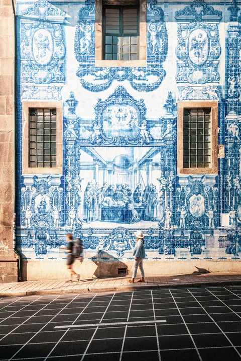 woman walking in porto against blue and white azulejos tile wall of the capela das almas church in porto