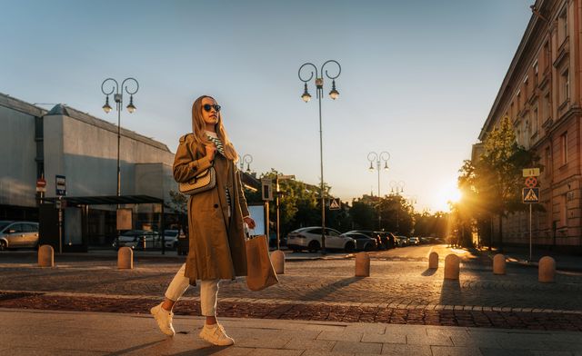 woman walks along city street in evening after shopping with paper bag