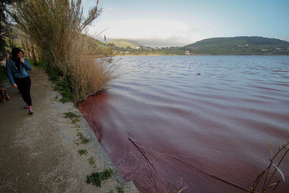 a woman walks near the red waters of lake averno