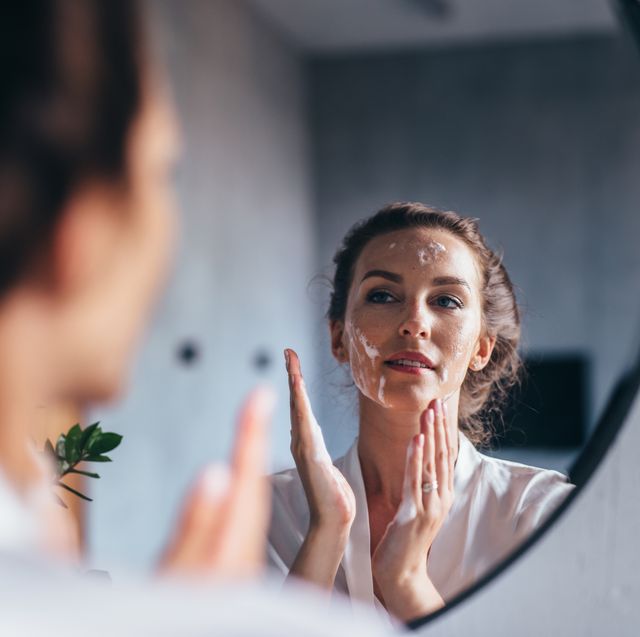 woman washes in front of the mirror, applying foam to her face