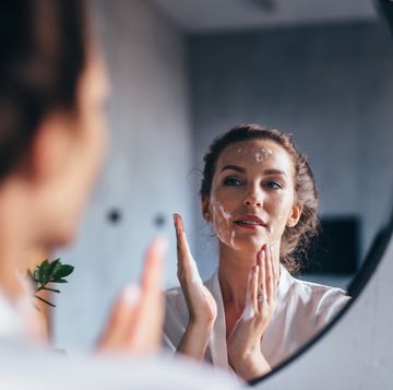 woman washes in front of the mirror, applying foam to her face
