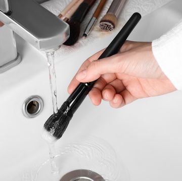 person washing makeup brush under stream of water in sink