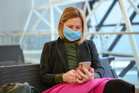 woman wearing a protective face mask and using a mobile phone at the airport stock photo