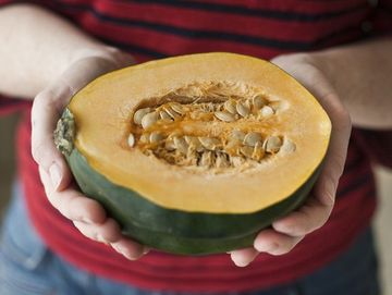 A woman wearing a red striped shirt holds out half of an organic acorn squash in her kitchen in Seattle, Washington.