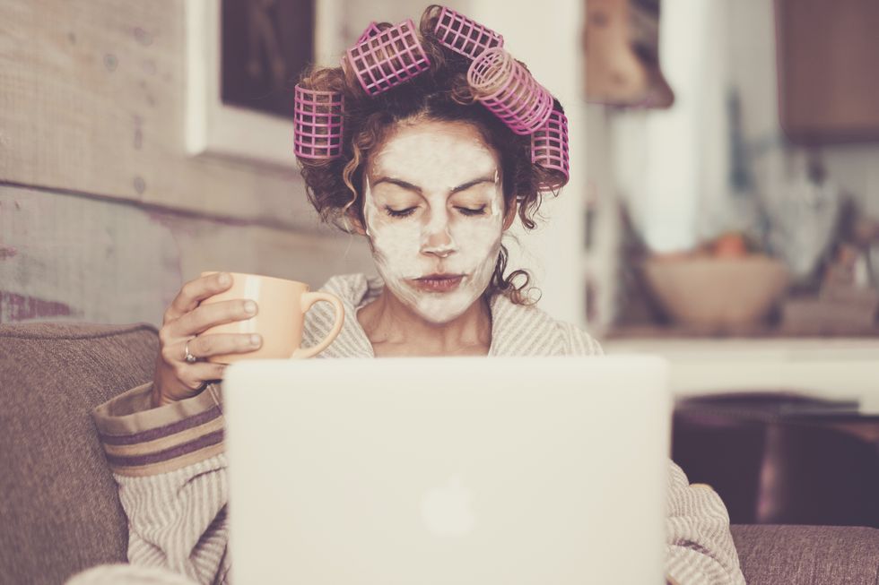 woman wearing hair curlers and face mask while using laptop at home