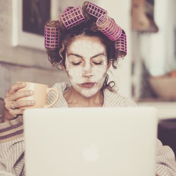 woman wearing hair curlers and face mask while using laptop at home