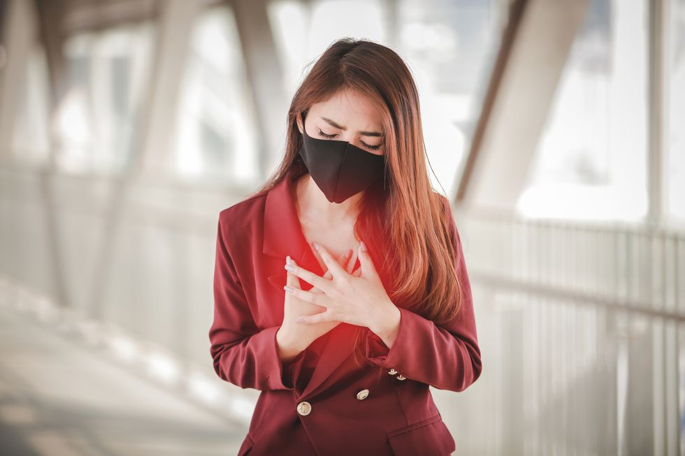 woman wearing mask touching chest while standing on footbridge
