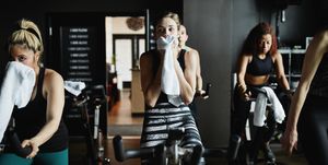 woman wiping sweat from face with towel during indoor cycling class in fitness studio