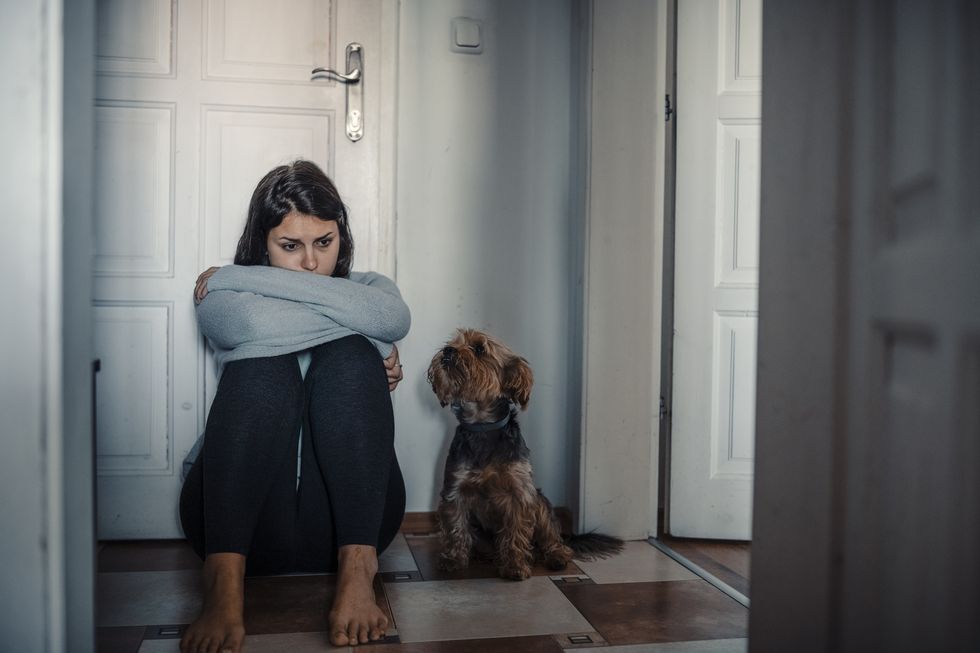 woman with a mental problems is sitting exhausted on the floor with her dog next to her