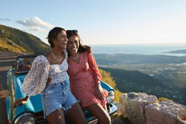 woman with arm around female friend leaning on car