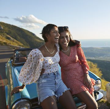 woman with arm around female friend leaning on car