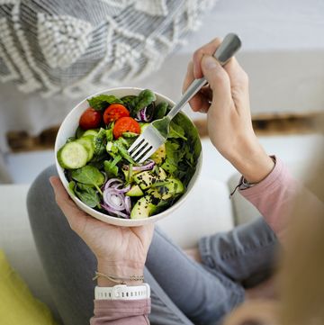woman with bowl of salad sitting on sofa at home