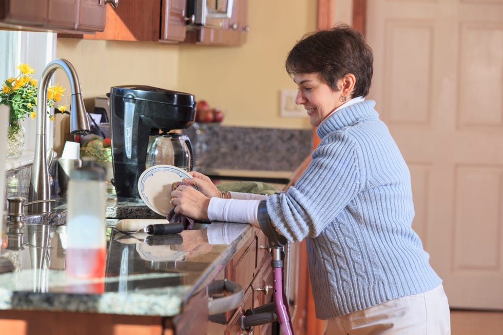 woman with cerebral palsy using crutches and washing dishes in her kitchen