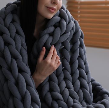 woman with chunky knit blanket in armchair at home, closeup