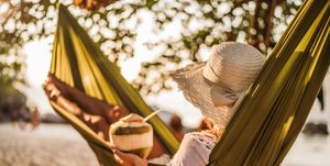 Woman with coconut drink relaxing in hammock at the beach.