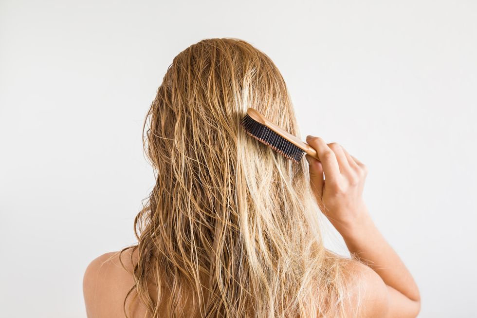 woman with comb brushing her wet blonde hair after shower on the gray background cares about a healthy and clean hair beauty salon concept