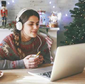 woman with cup of coffee using laptop and headphones at christmas time