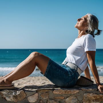 woman with eyes closed sitting on promenade at beach