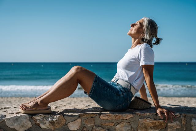 woman with eyes closed sitting on promenade at beach