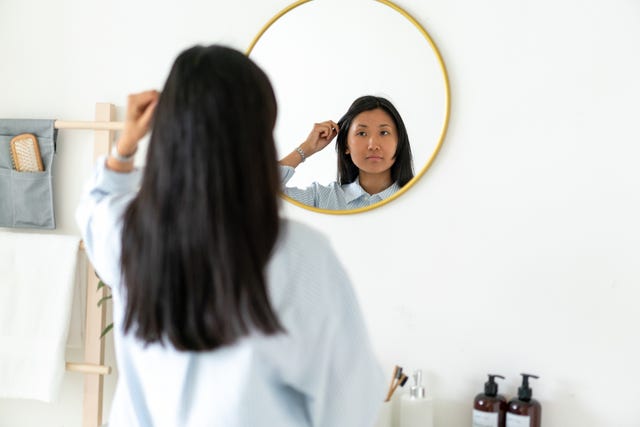 woman examining her hair loss in a bathroom mirror