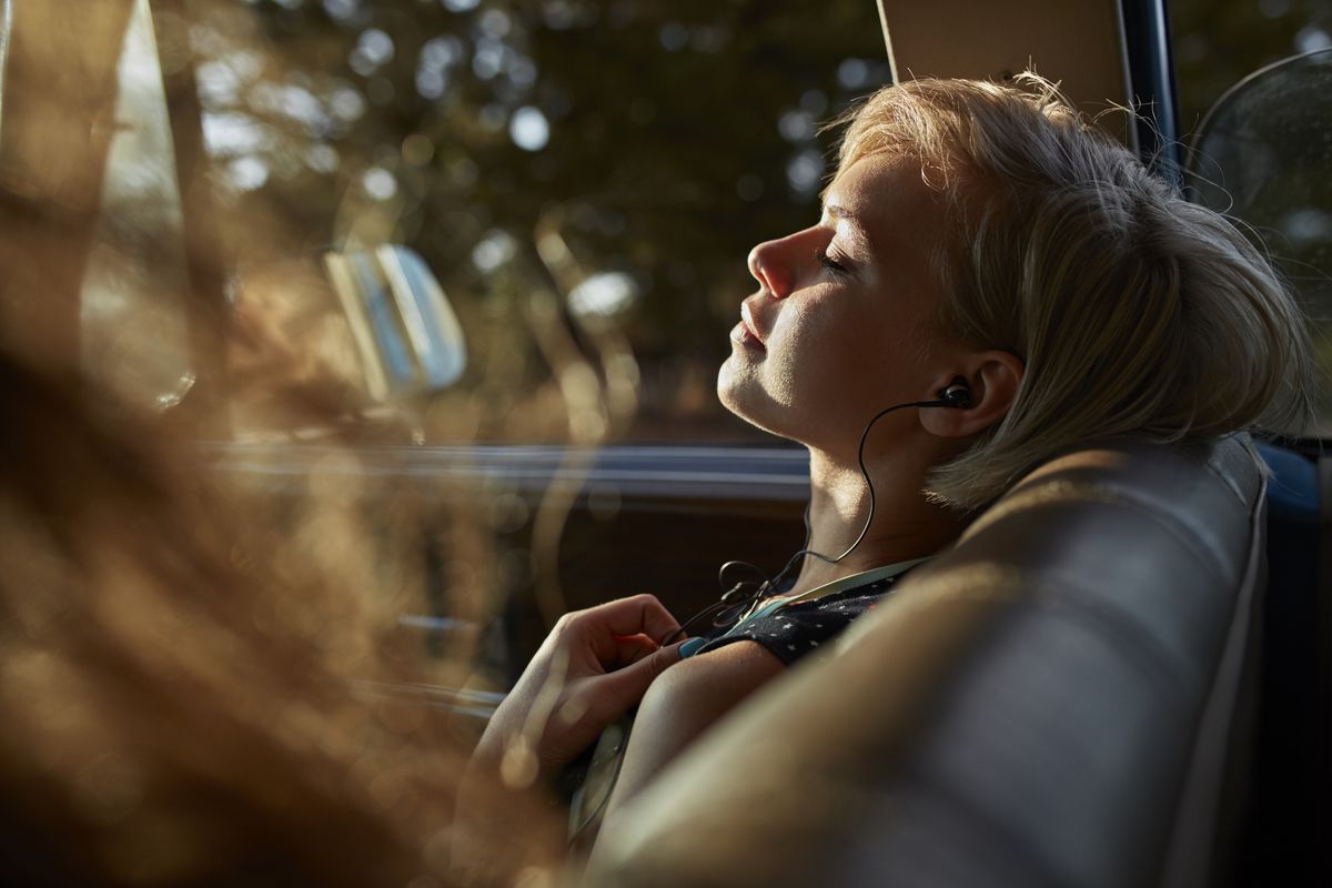 woman with headphones relaxing in car, at sunset