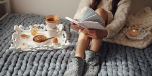 woman with long hair drinking hot coffee and reading book in bed woman in woolen socks and sweater sitting on wool chunky merino plaid cozy winter morning concept