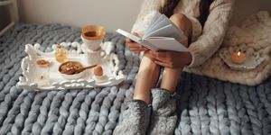 woman with long hair drinking hot coffee and reading book in bed woman in woolen socks and sweater sitting on wool chunky merino plaid cozy winter morning concept