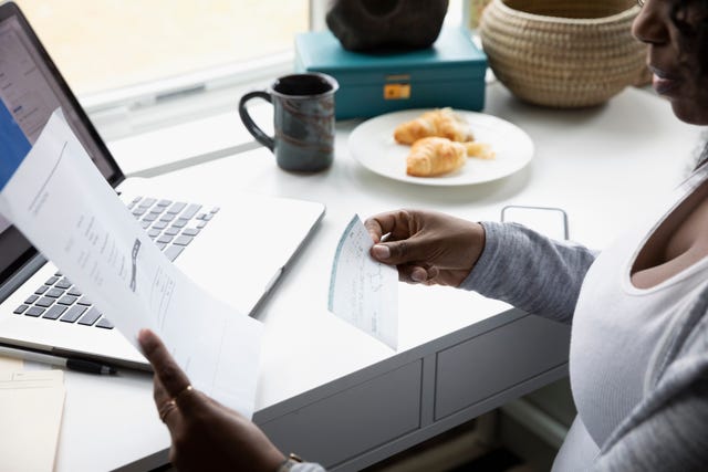 Woman with paperwork and check electronic banking at laptop