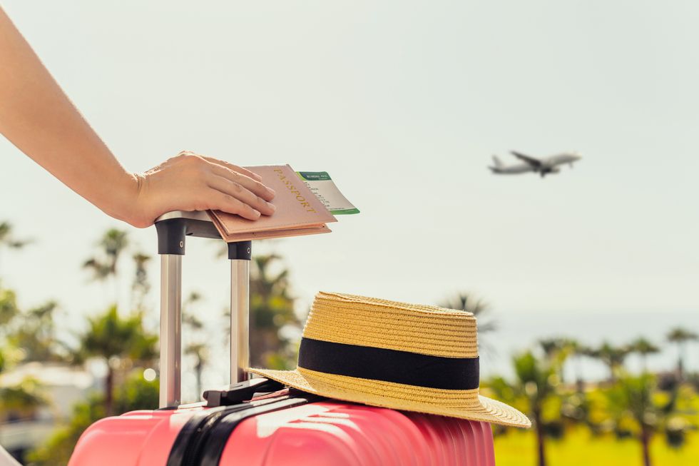 woman with pink suitcase and passport with boarding pass standing on passengers ladder of airplane opposite sea with palm trees tourism concept