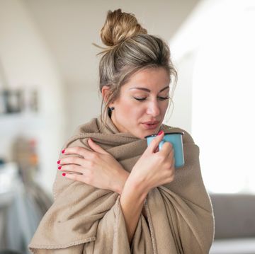woman wrapped having drink while standing at home