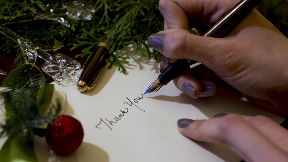 woman writing christmas card writing thank you with evergreen and ornaments background