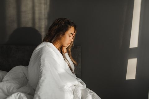 woman yawning and can't wake up in morning sitting in bed covered with blanket