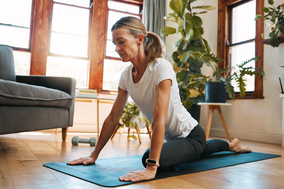 woman, yoga and pigeon pose stretching in house or home living room for relax exercise, training and workout in germany lockdown zen, calm and mature peace yogi in mind wellness and fitness for hips